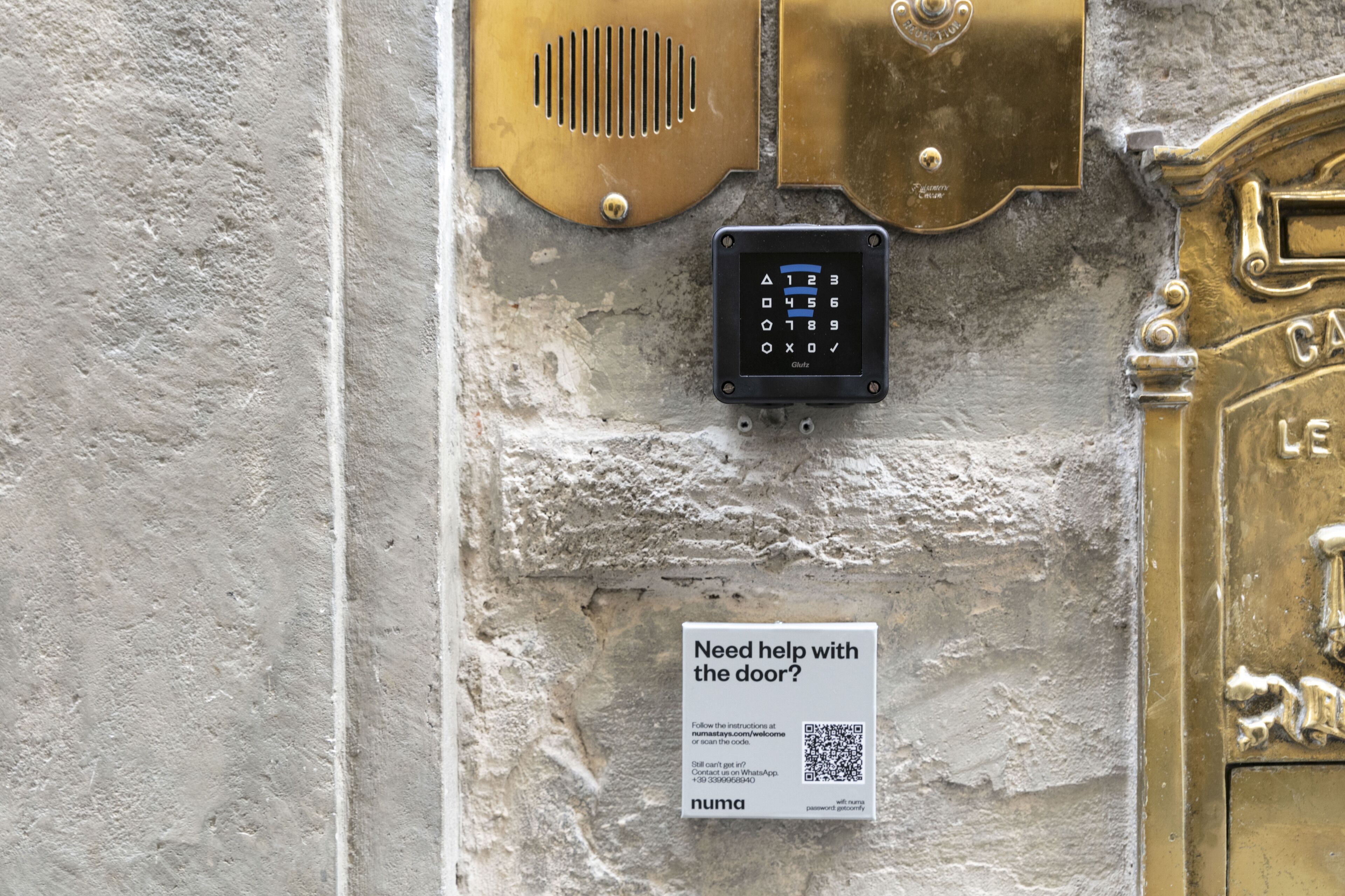 A keypad door lock with a sign offering help with the door, a QR code, and a brand name 'numa'.