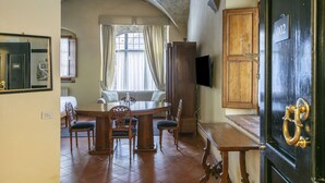 A dining area with a round table and chairs, a television on the wall, and a wooden cabinet with a brass handle. - Numa Florence Palazzo Belfiore (Florence)