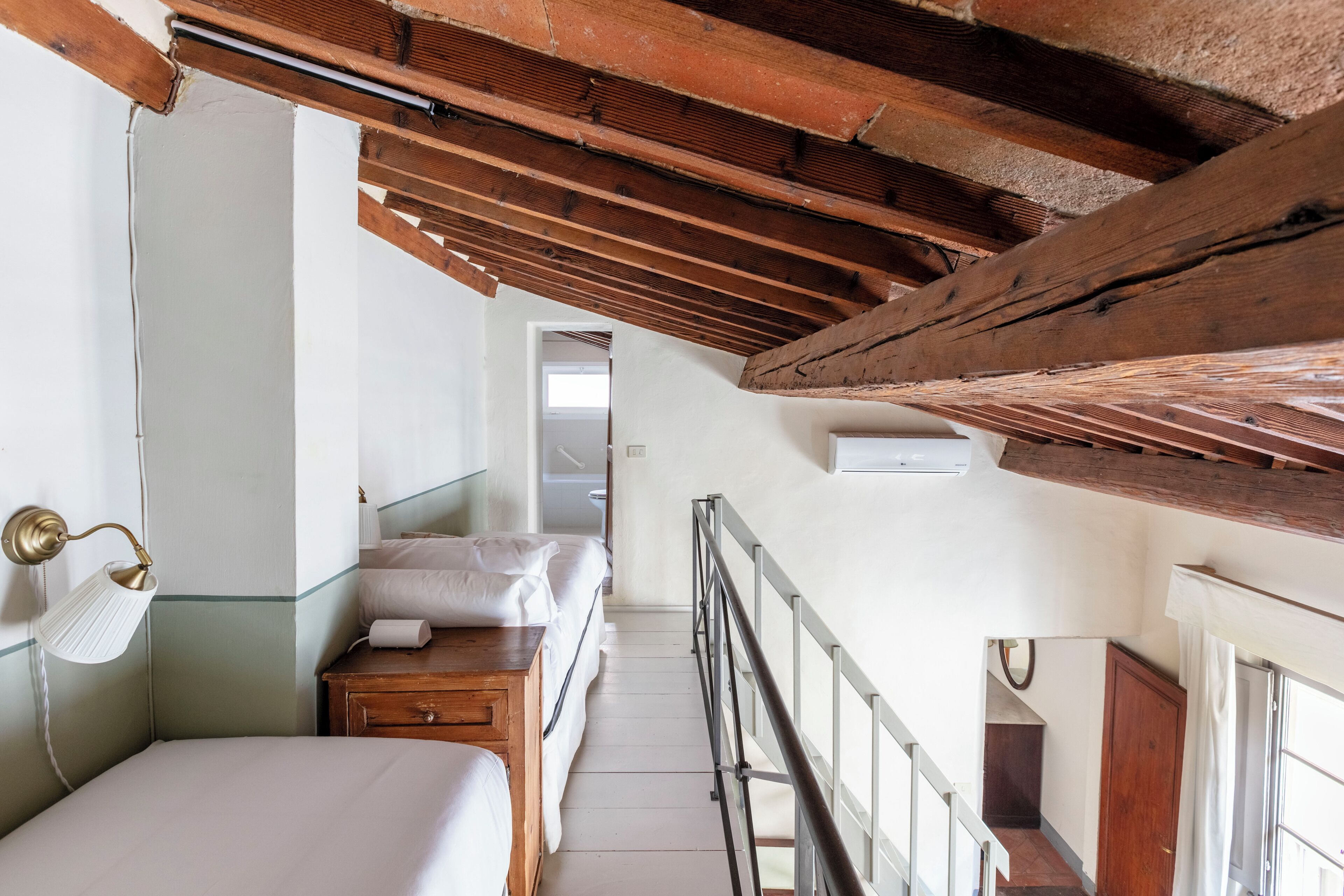 Un dormitorio con techo de madera, cama, mesita de noche, lámpara y ventana.