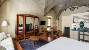 A bedroom with a bed, a wooden wardrobe, a desk with a chair, and a kitchenette area.