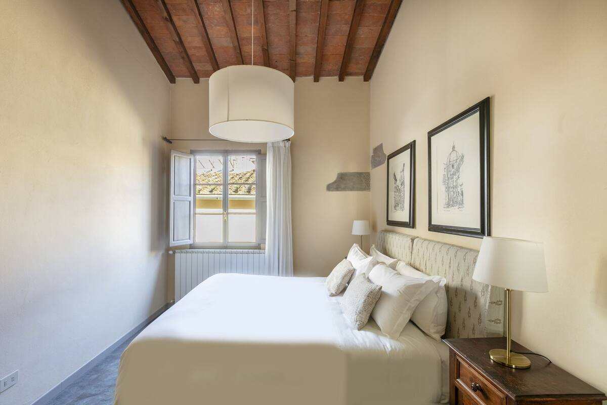 Un dormitorio con una cama grande, techo de madera, ventana con cortinas e imágenes enmarcadas en la pared.
