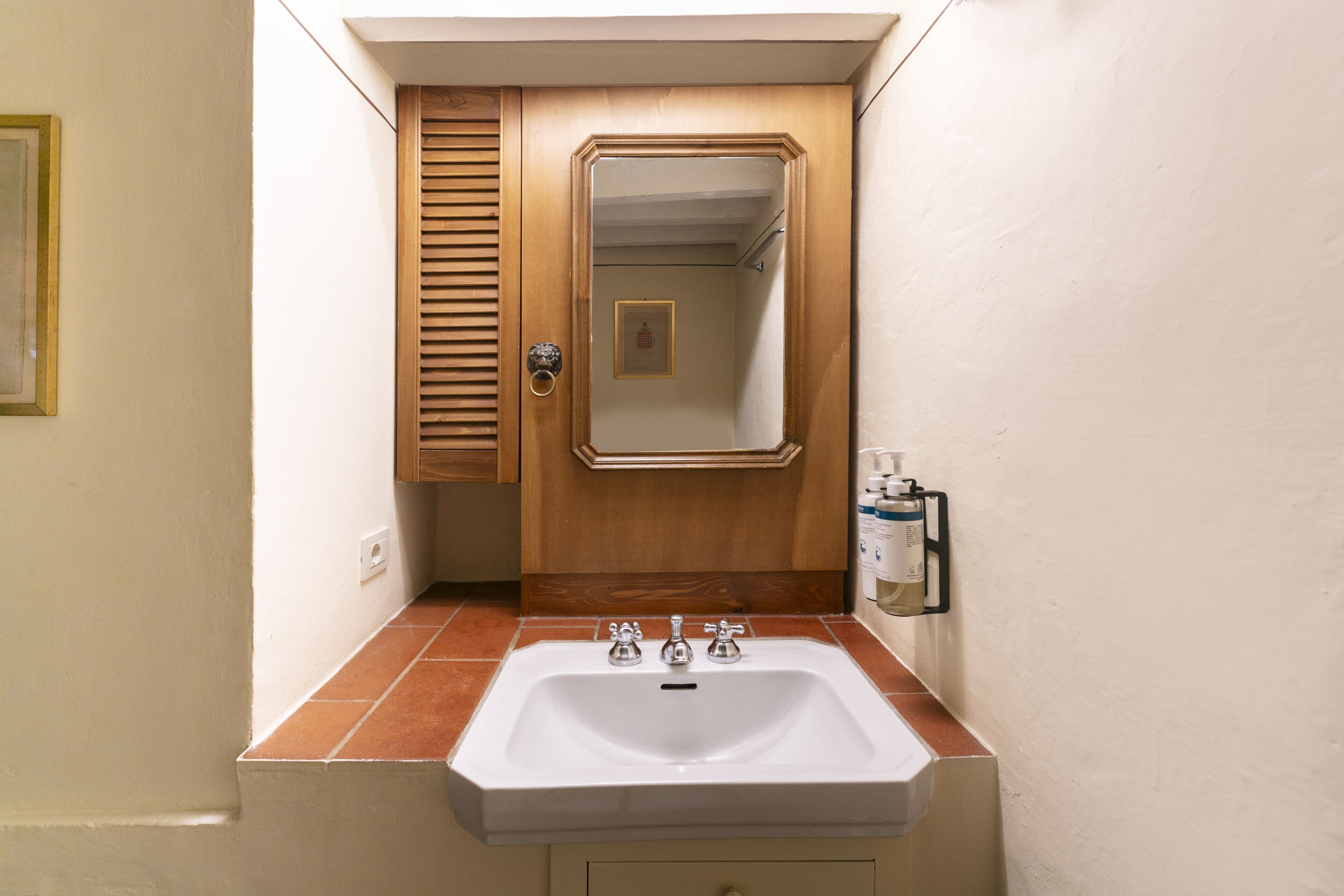 Un baño con lavamanos blanco, mueble de madera y espejo.