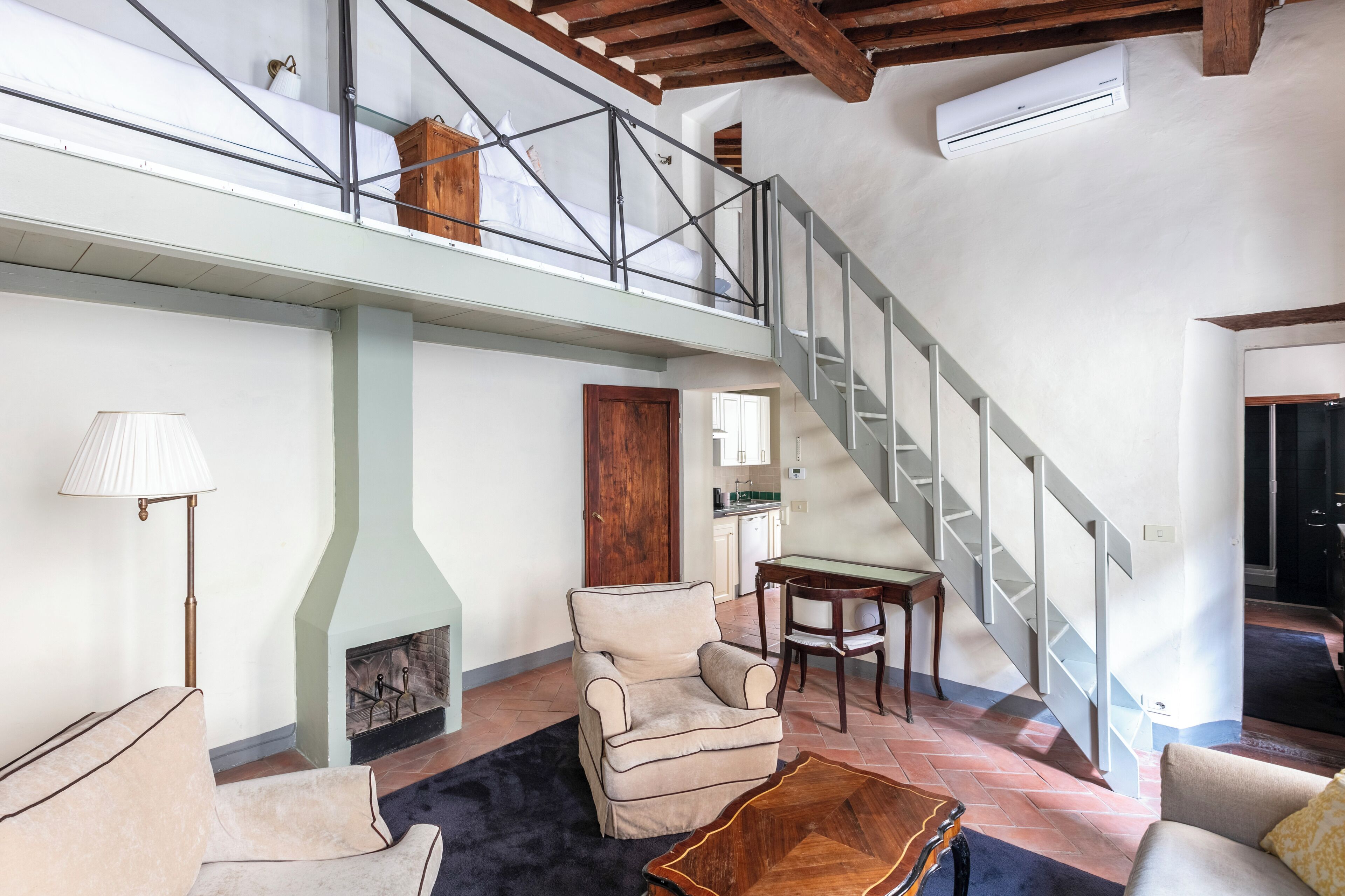 Un vaste espace de vie doté d’une cheminée, d’un plafond haut avec des poutres apparentes, d’un escalier et d’une vue sur un niveau supérieur.