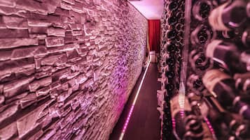 A corridor with a textured stone wall, a red curtain, and rows of musical instruments.