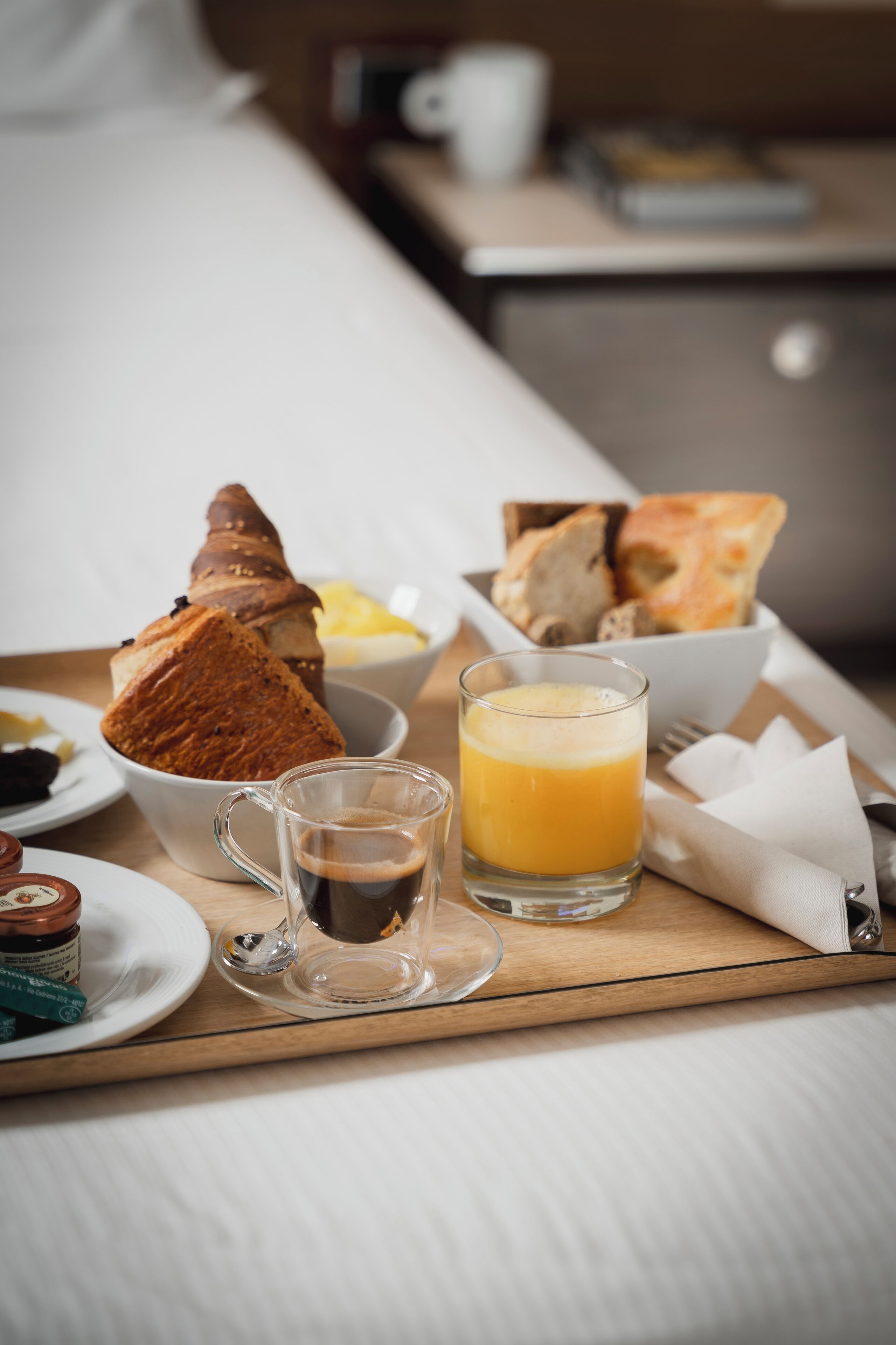 A breakfast tray with croissants, bread, a glass of orange juice, and a cup of coffee on a bed.
