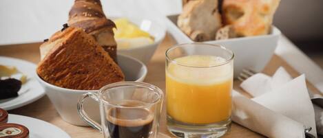 A breakfast tray with croissants, bread, a glass of orange juice, and a cup of coffee on a bed.