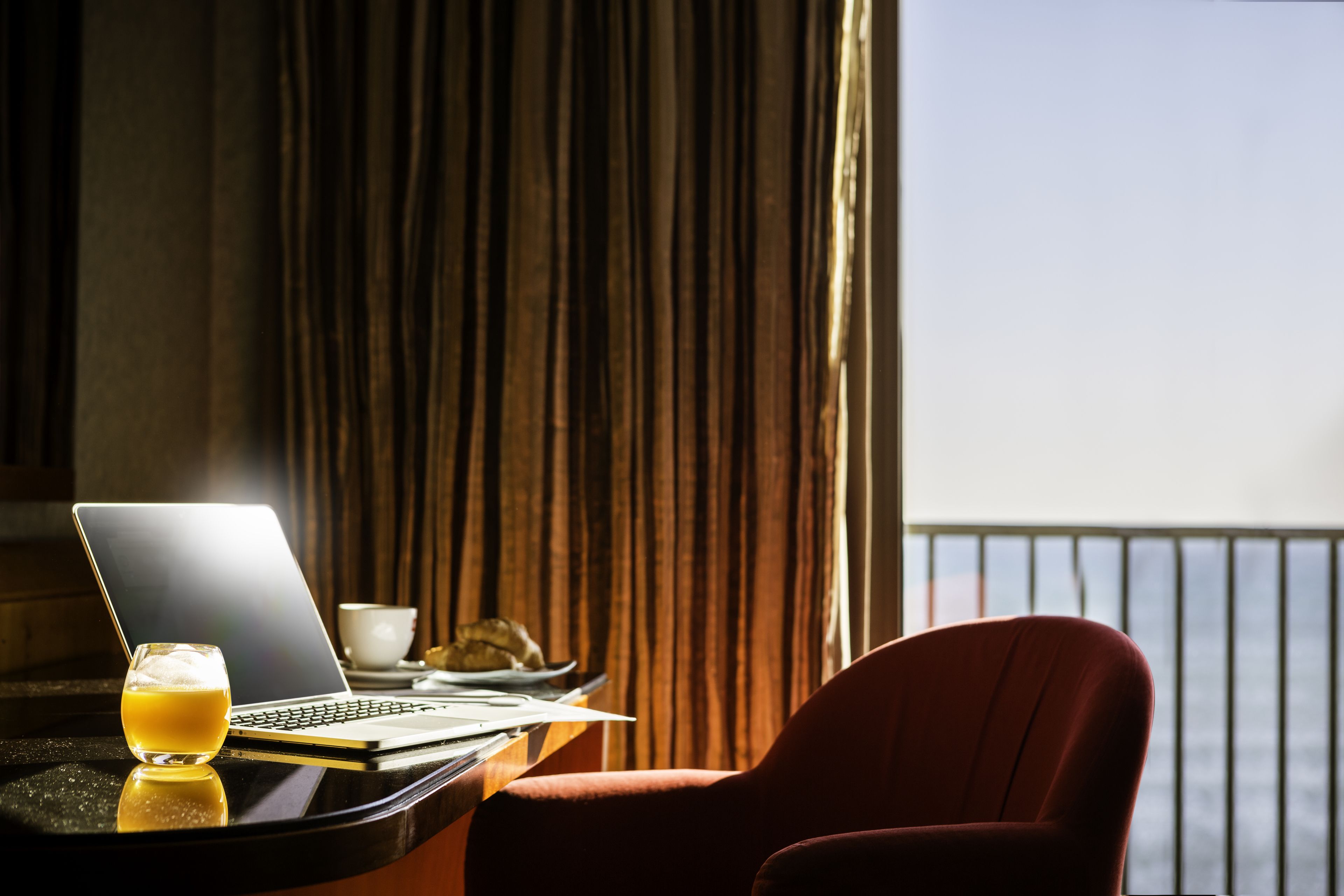 A laptop on a table with a glass of orange juice, a cup, and a plate of food.