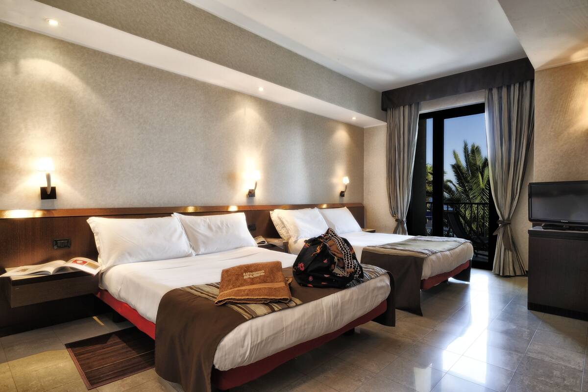 A hotel room with two beds, a TV, a desk, and a window with curtains.