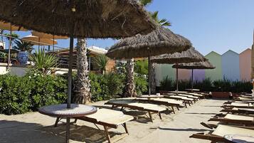 A beachside area with thatched umbrellas, lounge chairs, and a sandy ground.