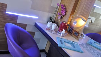 Una moderna camera d'albergo con una reception, poltrone viola, una macchina per caffè e una pianta di orchidea decorativa.