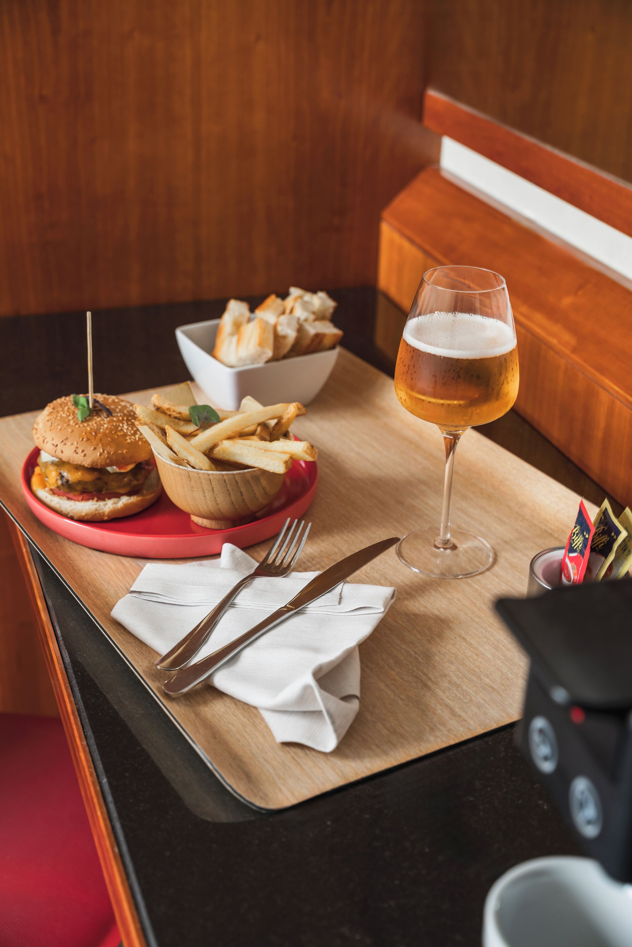 A meal setup with a burger, fries, and a glass of beer on a wooden table.