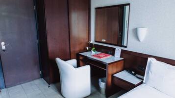 A hotel room with a bed, a desk, a chair, a mirror, and a wardrobe.
