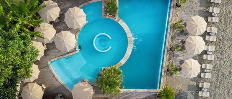 Vista aérea de uma área de piscina com um elemento aquático circular, rodeada por espreguiçadeiras e guarda-sóis.
