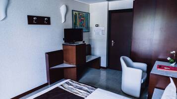 Ett hotellrum med en säng, ett skrivbord, en stol, en tv och en dörr.