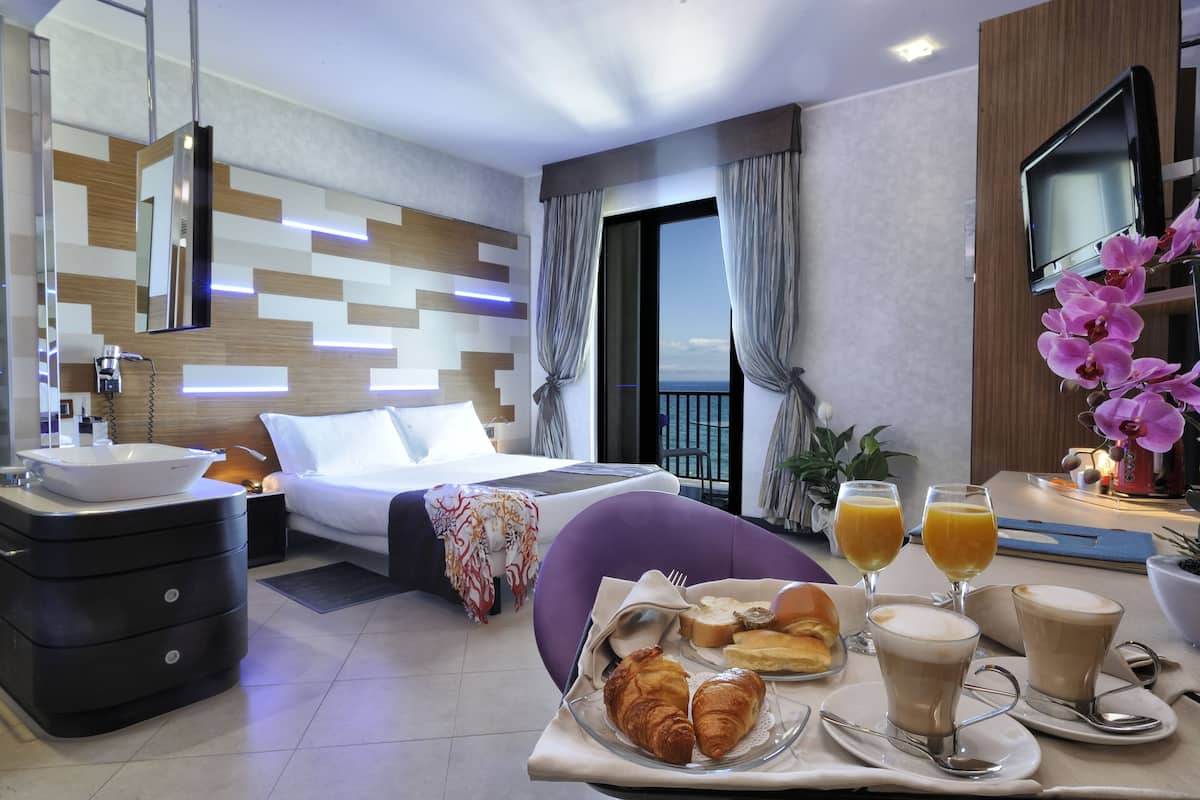 A modern hotel room with a bed, bedside table, and a breakfast tray with croissants, juice, and coffee.