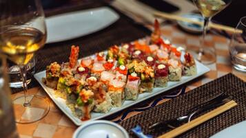 Una bandeja de sushi sobre una mesa con palillos, un tazón pequeño y copas de vino.