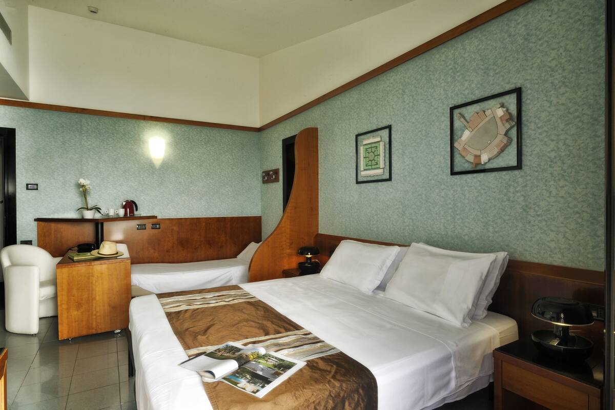A hotel room with two beds, a wooden headboard, a desk with a chair, a nightstand, and framed artwork on the wall.