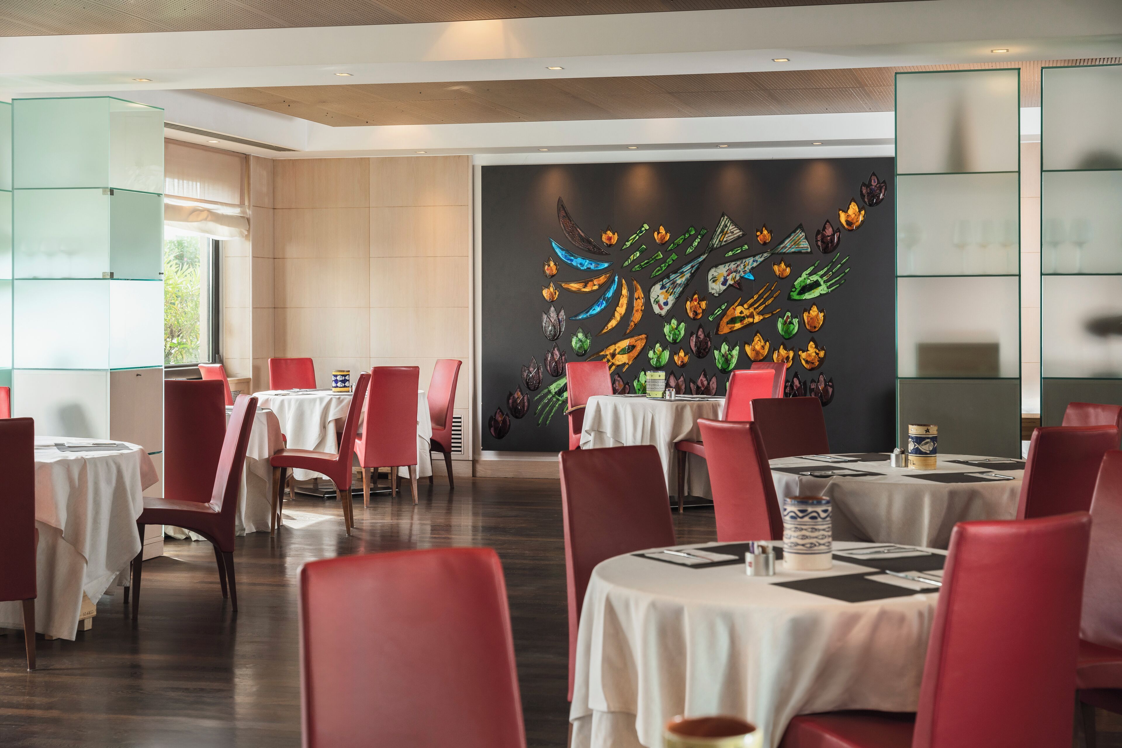 A restaurant with red chairs and white tablecloths, a black wall with colorful artwork, and a glass display case.
