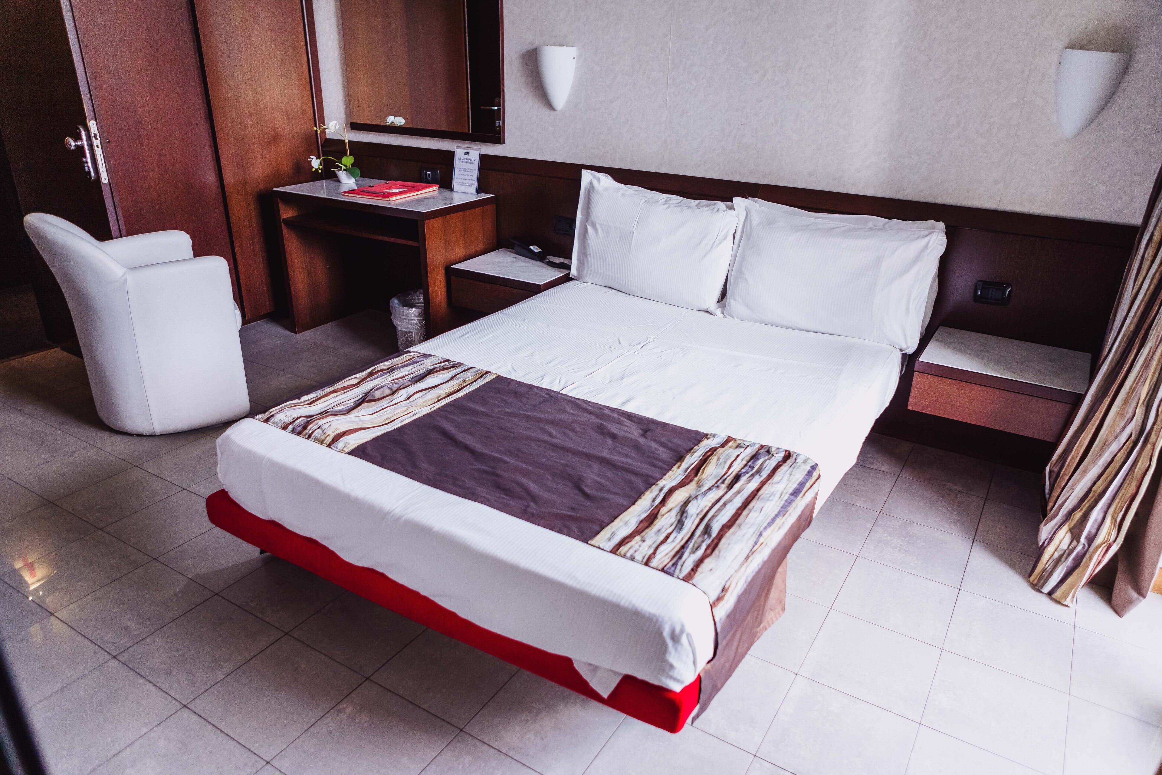 A hotel room with a large bed, a desk, a chair, a nightstand, and a mirror.