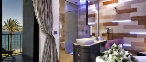 A modern bathroom with a glass shower enclosure, a vanity with a large sink, and a view of the ocean through a balcony.