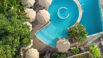 An aerial view of a swimming pool with a circular design, surrounded by palm trees and umbrellas.