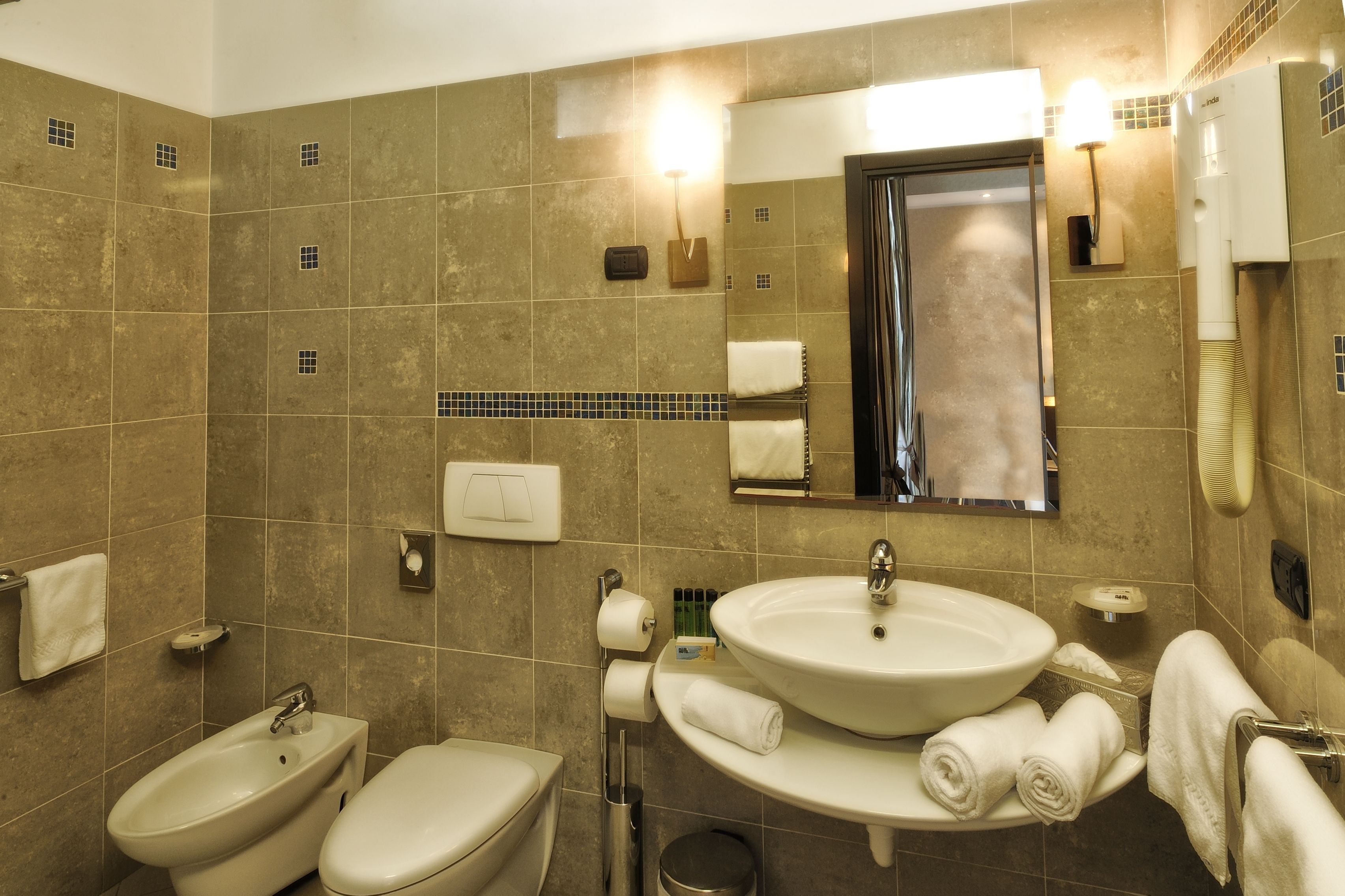 A bathroom with a bidet, toilet, sink, and mirror.