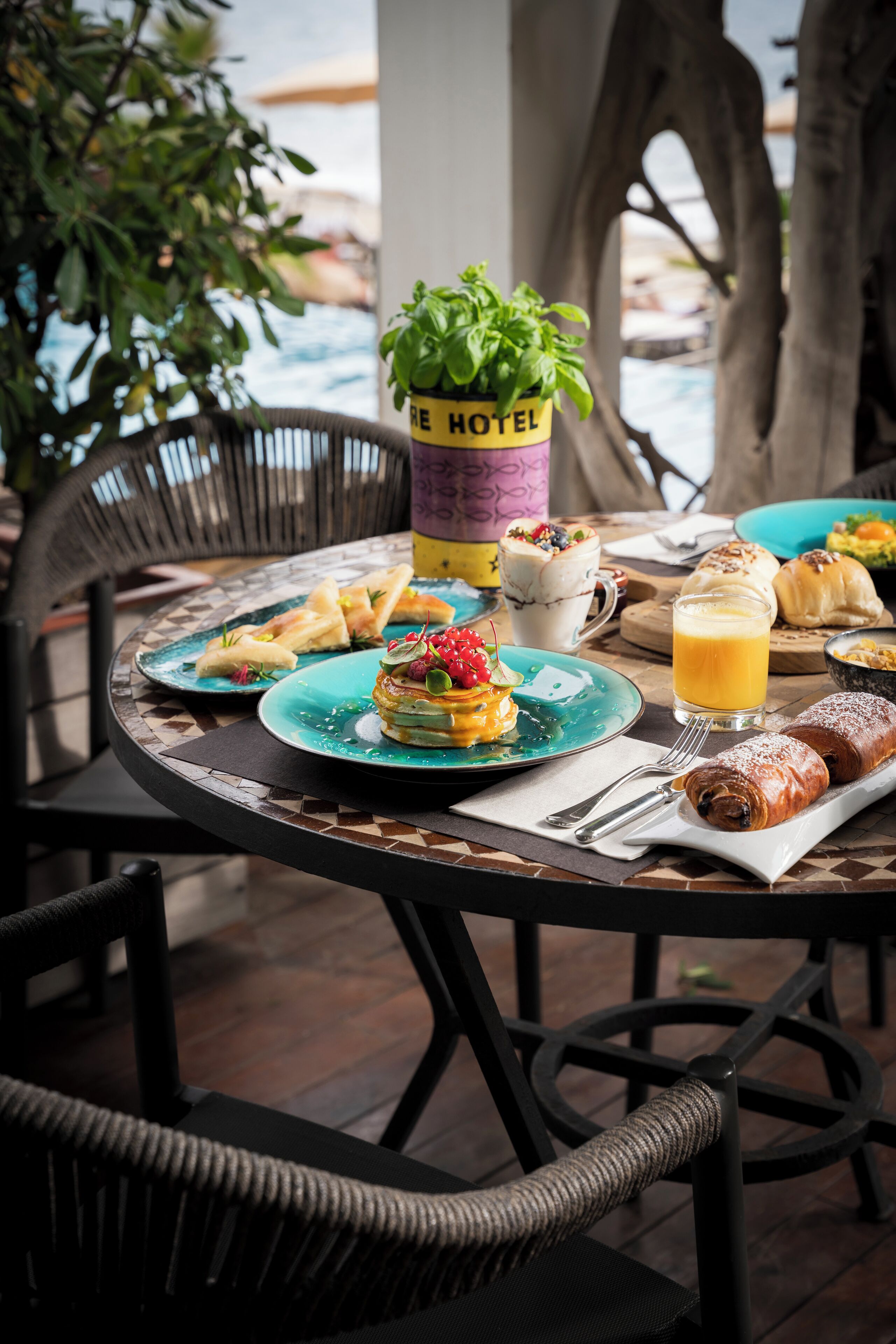 Una mesa de comedor con alimentos para el desayuno, una planta en maceta y un cartel que dice "RE HOTEL".