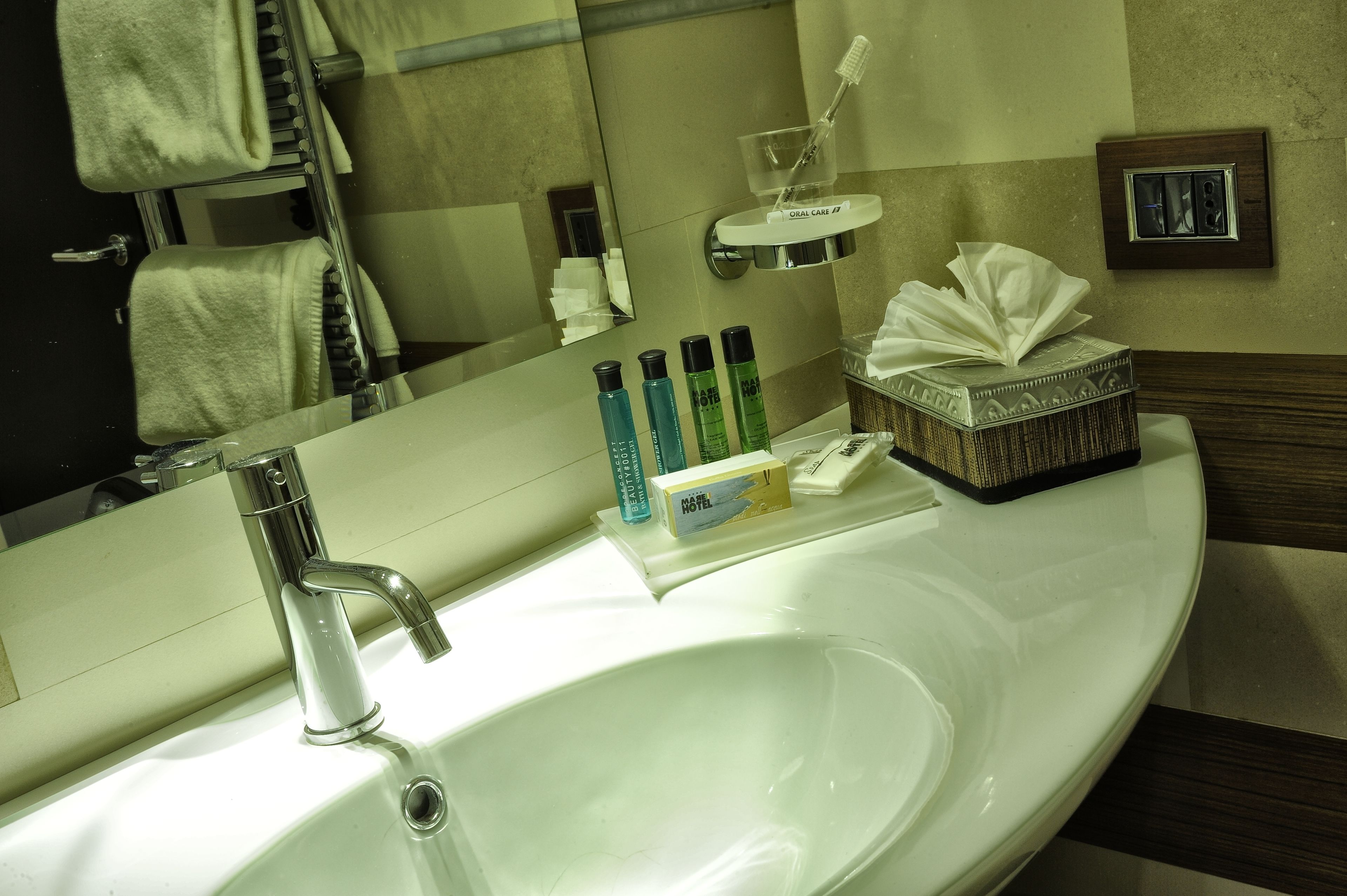 Une salle de bain d’hôtel avec un lavabo blanc, un miroir, un porte-serviettes et des articles de toilette.