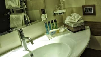 Une salle de bain d’hôtel avec un lavabo blanc, un miroir, un porte-serviettes et des articles de toilette.