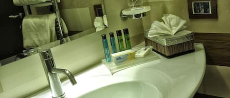 Une salle de bain d’hôtel avec un lavabo blanc, un miroir, un porte-serviettes et des articles de toilette.