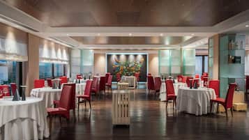 A spacious dining area with round tables and red chairs, a central decorative wall, and a view of the outdoors.