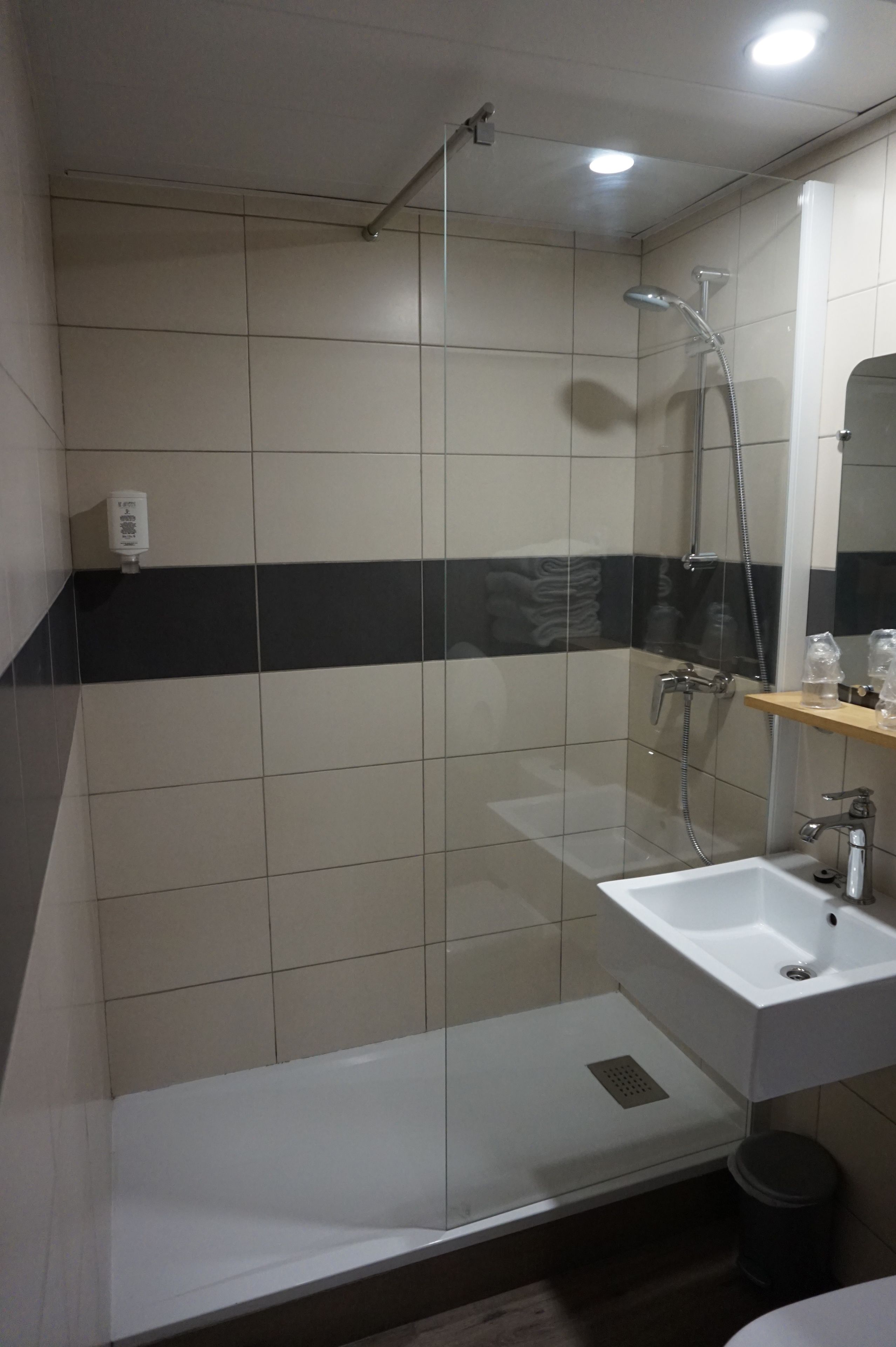Un baño moderno con ducha de vidrio, lavamanos blanco y un espejo encima.