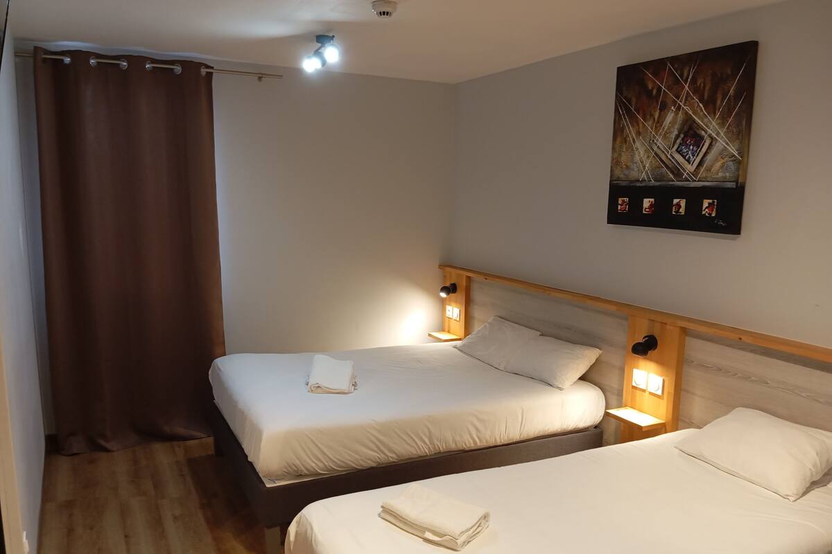 A hotel room with two beds, a wooden headboard, a painting on the wall, and a curtain.