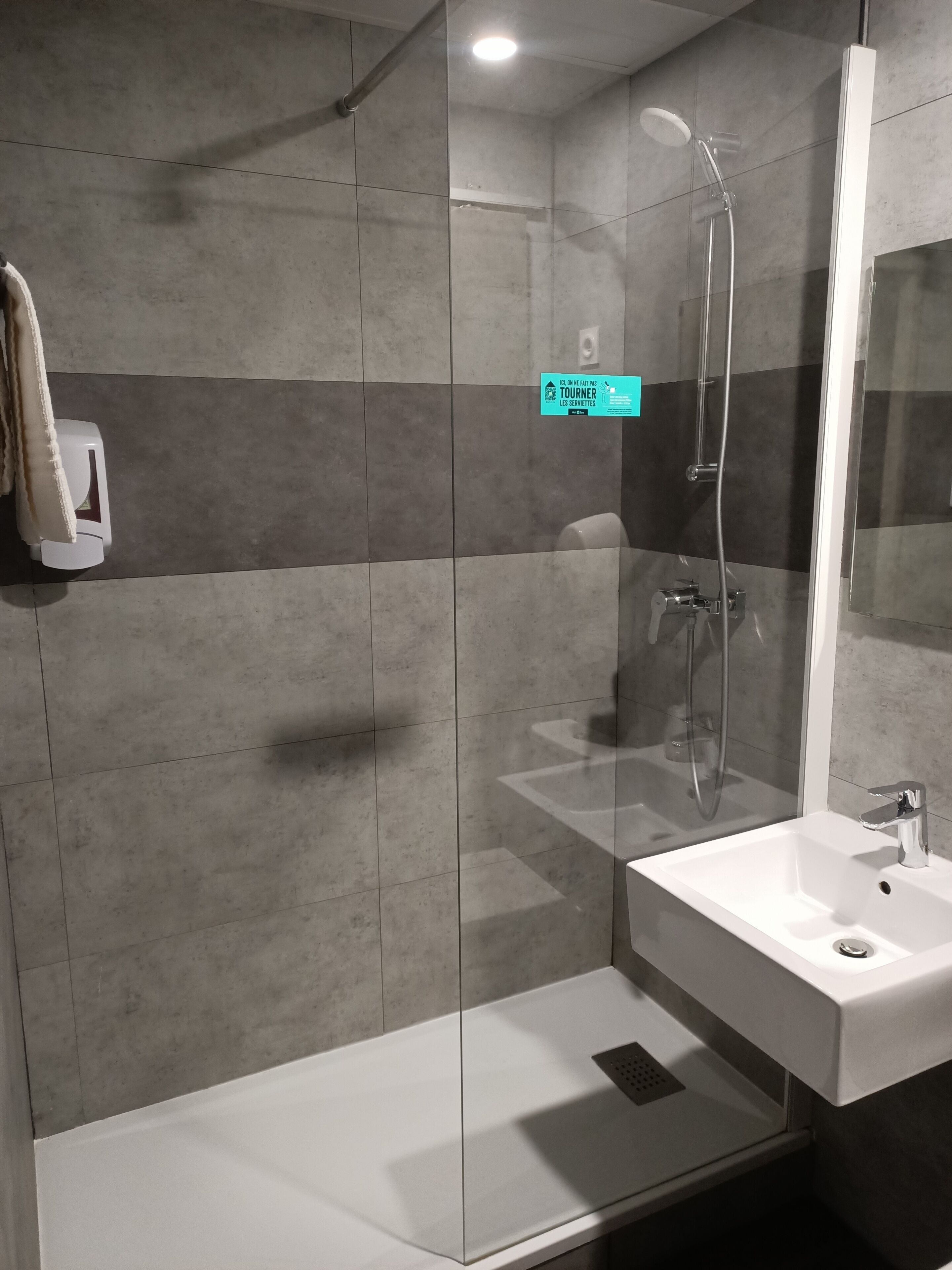Une salle de bain moderne avec une douche à parois de verre, un lavabo blanc et un distributeur de serviettes.