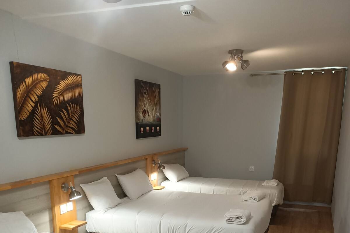 A hotel room with three single beds, wooden headboards, and a ceiling light.