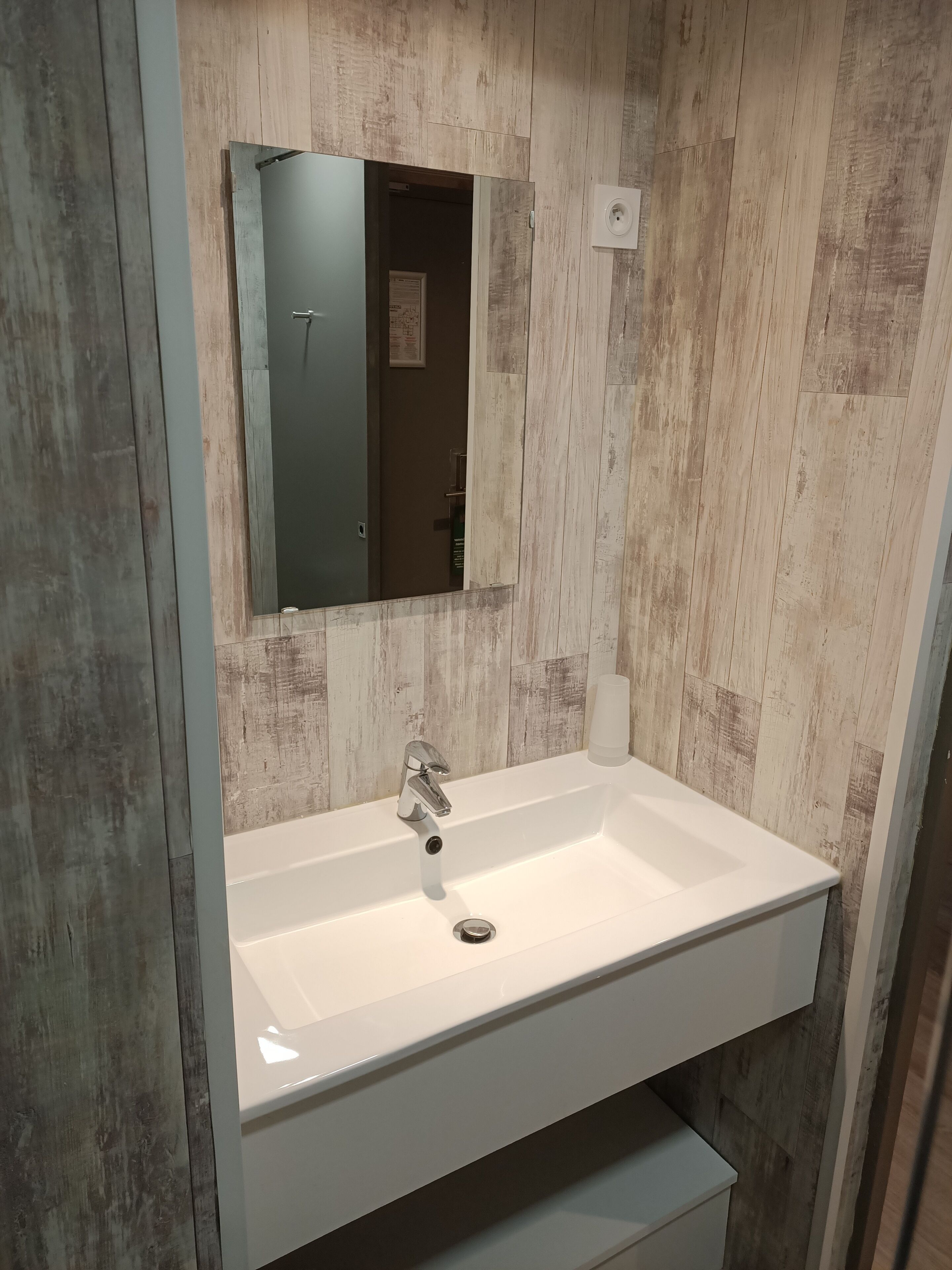A bathroom with a white sink, a mirror, and a wooden wall.
