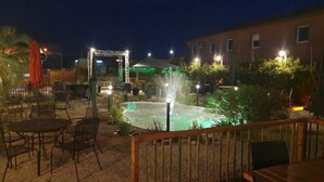 An outdoor patio area with tables and chairs, a small fountain, and a building in the background. - Logis Hôtel Acotel (Le Pontet)