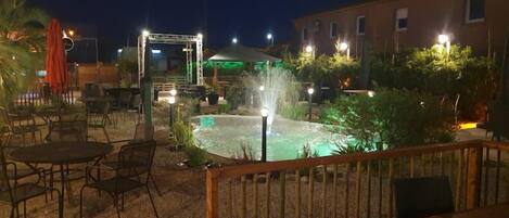 An outdoor patio area with tables and chairs, a small fountain, and a building in the background.