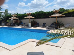 Una piscina con sillas de descanso y sombrillas de paja.