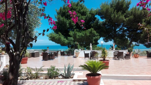 An outdoor terrace with tables and chairs, potted plants, and a view of the sea. - Residence Maresol (Vieste)