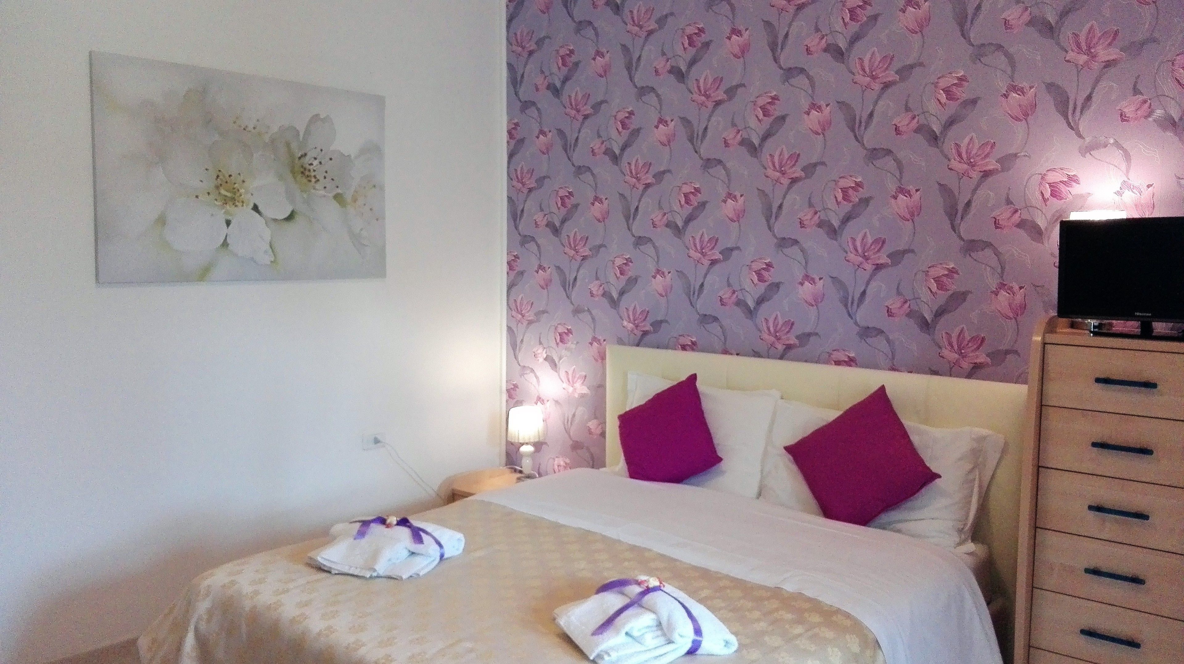 Una camera d'albergo con un letto, un comodino, una televisione e una parete con carta da parati floreale.