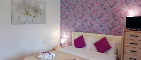 Una camera d'albergo con un letto, un comodino, una televisione e una parete con carta da parati floreale.