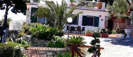 A two-story building with a balcony, stone wall, and potted plants.