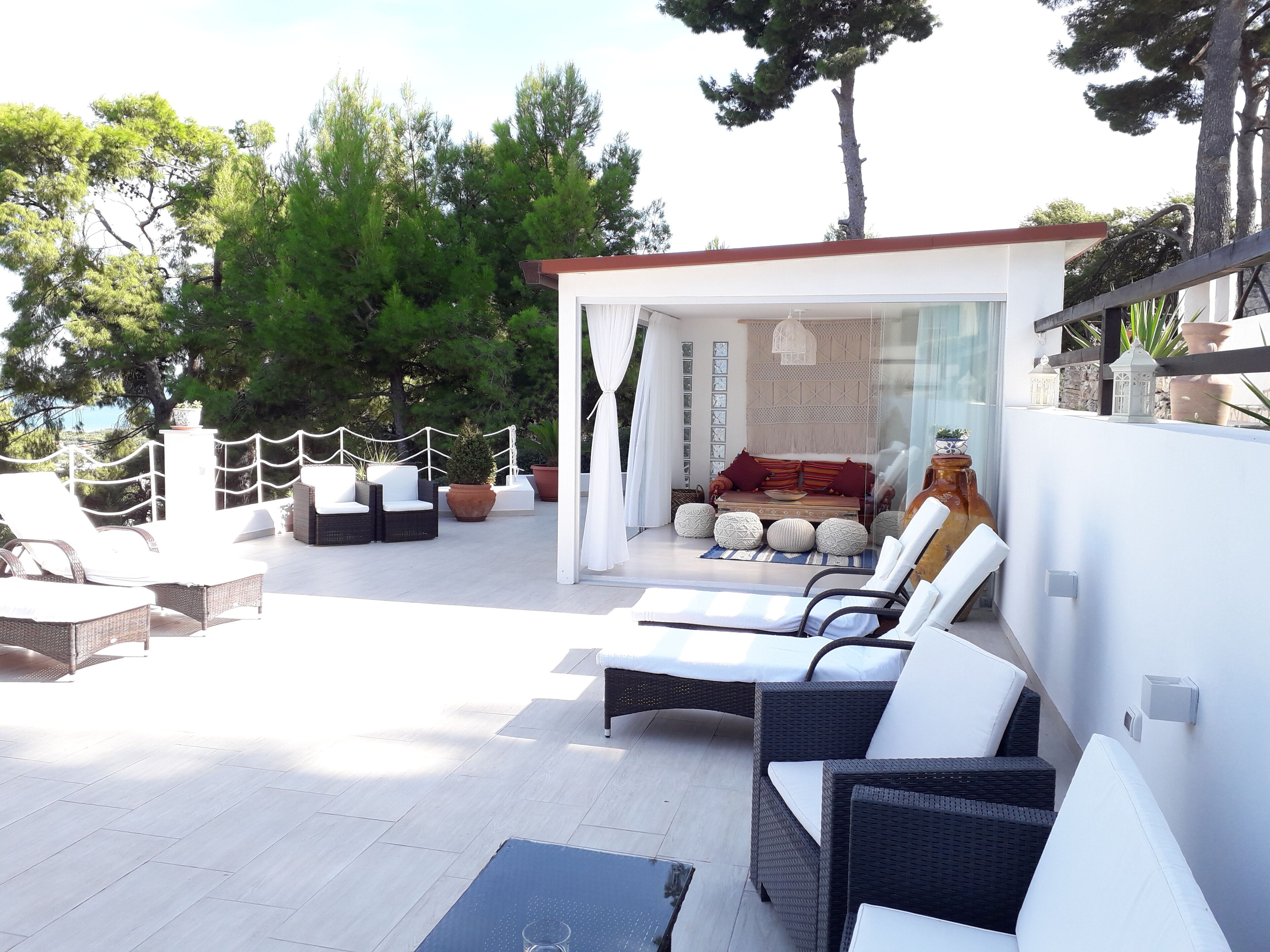 A sunlit outdoor lounge area with wicker furniture, a cushioned seating area, and potted plants.