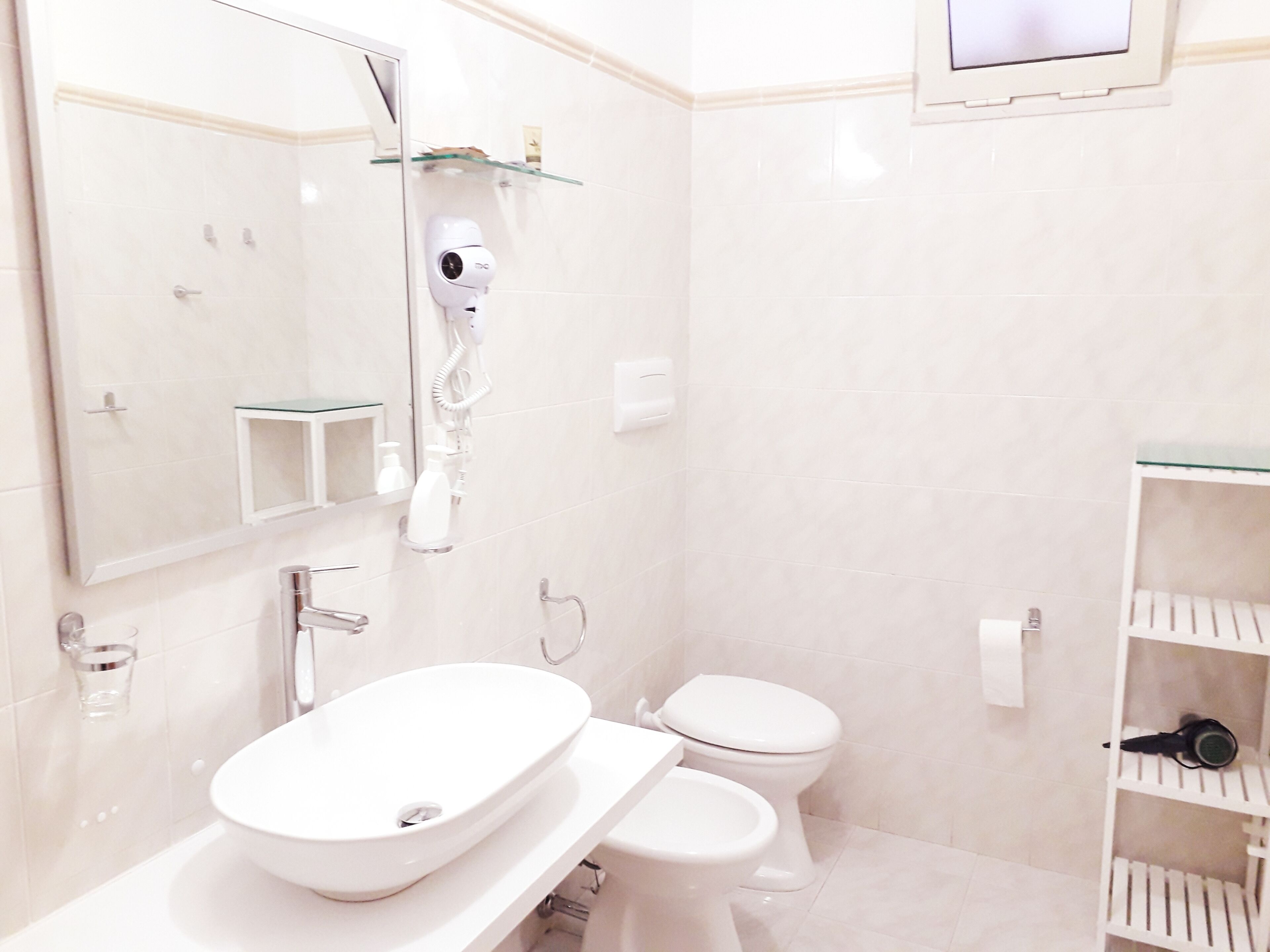 A modern bathroom with a large mirror, a white sink, a toilet, and a glass shelf with toiletries.