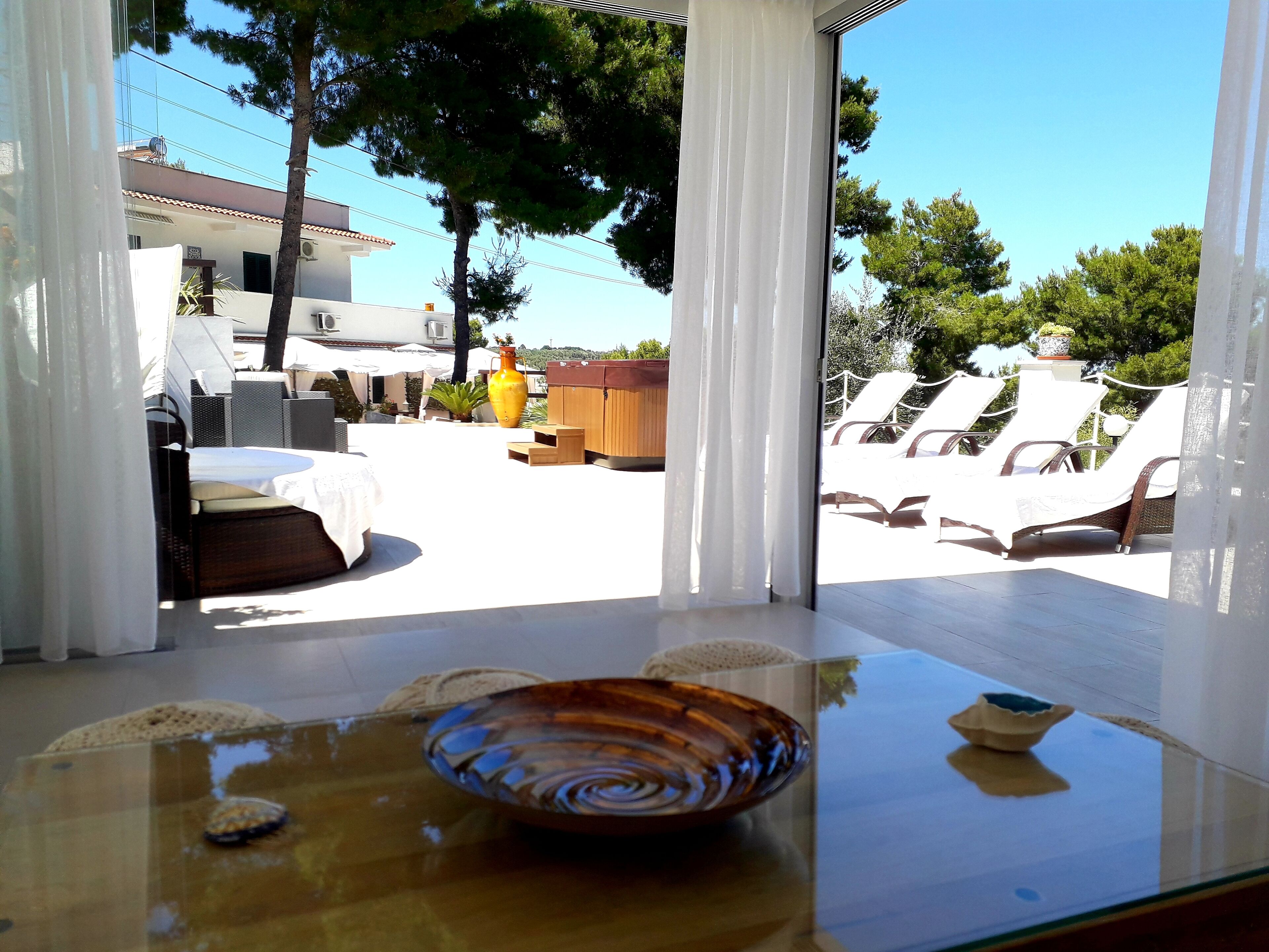 A sunlit patio with a glass table, a decorative bowl, and outdoor furniture.