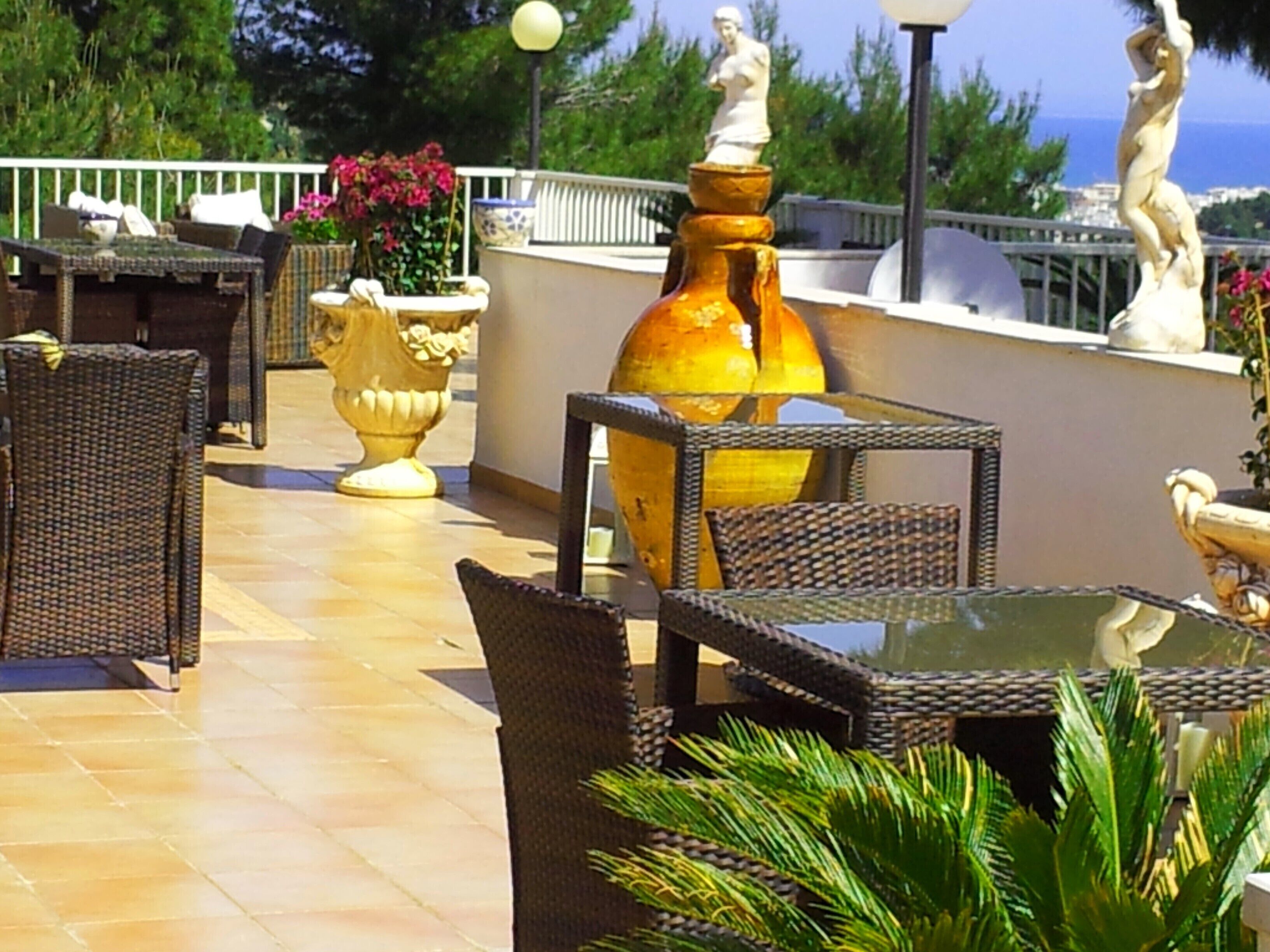 An outdoor patio with wicker furniture, a glass table, and decorative vases.