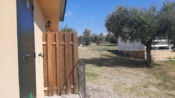 A wooden gate leading to a paved area with a tree and a white fence.