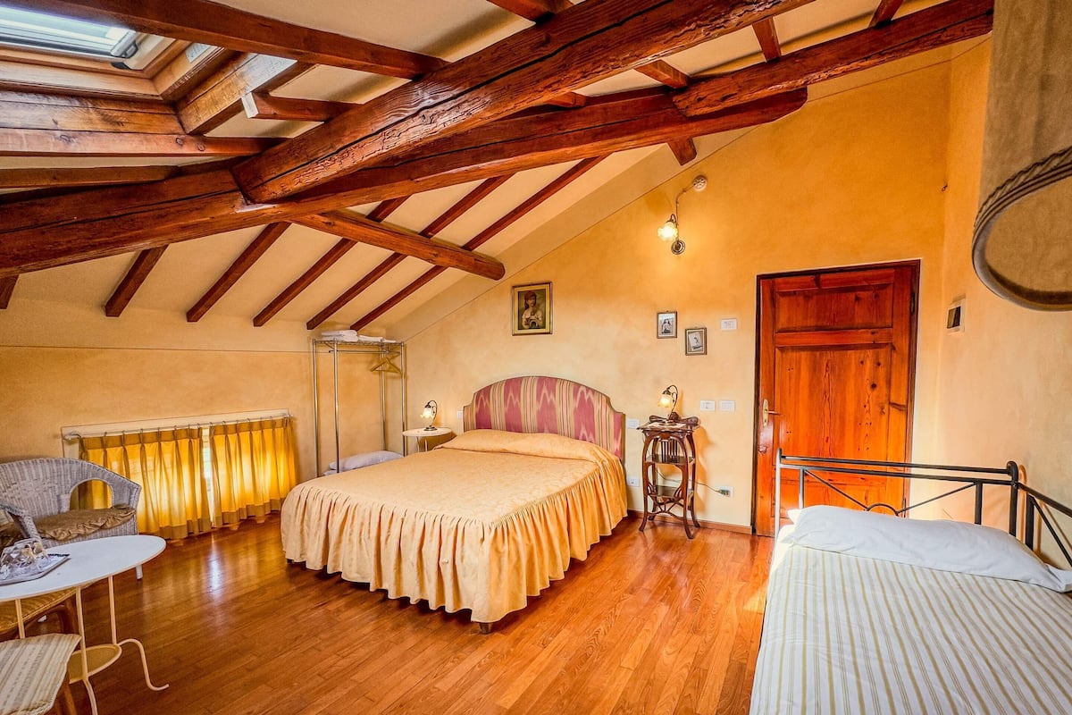 A bedroom with a large bed, a wooden ceiling, a small table, and a chair.