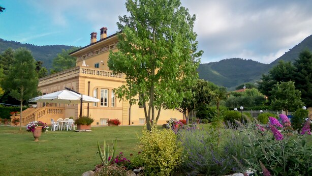 A large building with a balcony, surrounded by a well-maintained garden with various plants and flowers. - Marta Guest House (Lucca)